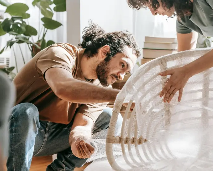 Homeowner preparing for pest treatment by wrapping a chair in bubble wrap for inspection and protection.