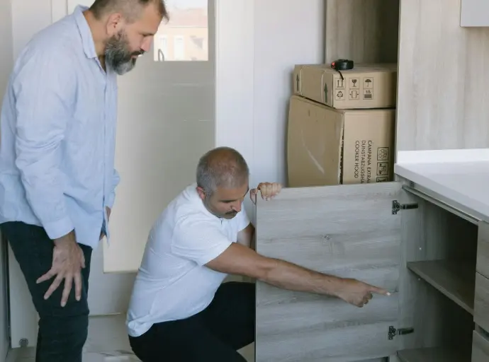 Pest control technician inspecting and pointing to a kitchen cupboard during a home assessment.